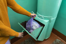 A Woman Throws A Bag Of Garbage Into A Garbage Chute At The Entrance Of An Apartment Building In Russia. Selective Focus