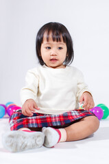 Wall Mural - Studio shot of little cute short black hair Asian baby girl daughter model in casual plaid skirt sitting on floor smiling laughing playing with colorful round balls toy alone on white background