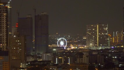 Poster - A ferris wheel in Bangkok, Thailand. Financial district and skyscraper buildings. Downtown skyline at night.