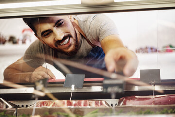 Wall Mural - Young man butcher arranging meat products in display case of butcher shop