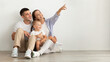 © Prostock-studio - Happy Young Family With Infant Baby Sitting On Floor And Pointing Aside
