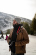 © MiguelAngelJunquera - Chico con barba en la nieve con camara de fotos con ropa marron