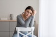 Leinwandbild Motiv Upset young woman sits alone, looking away with sad expression at home interior