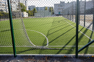 Lawn field for playing football behind the green fence mesh. Close-up of soccer field with green grass