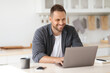 © Prostock-studio - Cozy work at home Young happy man independent contractor working on laptop and smiling, enjoying remote work