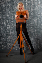 Adult Slim Blonde Woman Posing Next To An Old Vintage Wooden Gimbal Pavilion Camera