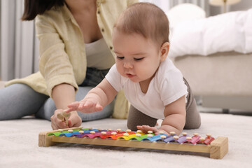 Poster - Cute baby and mother playing with xylophone on floor at home