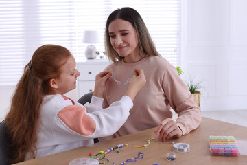 Poster - Happy mother with her daughter making beaded jewelry at home