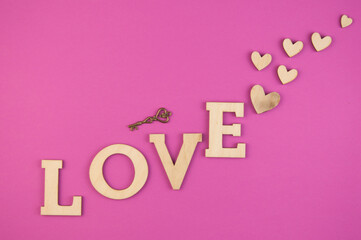 Wall Mural - The word Love with small hearts against a pink paper background closeup