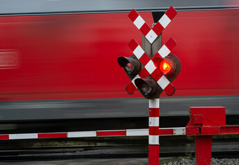 Wall Mural - Red freight train passes at crossing with red signal and closed barriers. 