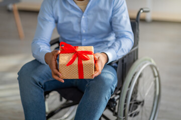 Wall Mural - Unrecognizable disabled black man in wheelchair holding gift box wrapped with red ribbon and bow at home