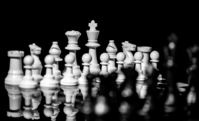 Close up of Chess pieces on a reflective mirror board surface with black background