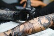 © Serhii - Cropped close up of a bearded tattoo artist working at his studio tattooing sleeve on the arm of his male client. Man getting tattooed by professional tattooist