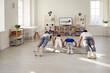 © Studio Romantic - Happy sporty family doing physical exercises at home. Mum, dad and kids practising push ups together while watching a video workout lesson with a gym fitness instructor on the TV screen, back view