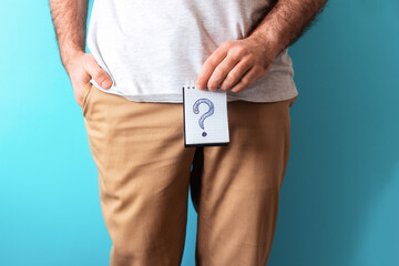 a man in beige jeans holds a notepad with question mark. close up. blue background. the concept of a