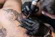 © alones - Male tattoo artist with black sterile gloves and a tattoo machine fills a tattoo, close-up
