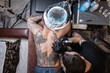 Professional tattoo master with a tattoo machine stuffs a knight's drawing on a man's back, top view. Workflow tattoo artists