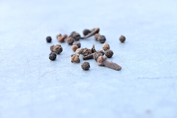 Sticker - A closeup of the bunch of black peppers with brown cloves on a blue surface