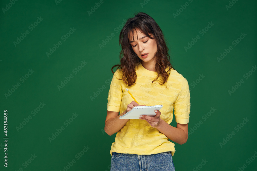 Pensive young girl writing startup business ideas, plans, creative thoughts to notebook, make to-do list not to forget