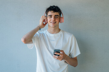 Wall Mural - teen boy with mobile phone and headphones listening to music isolated on wall with copy-space