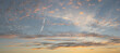 A skyscape with cirrocumulus clouds in white, red, yellow and grey and a clear deep blue sky at sunset in the summer
