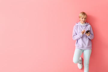 Wall Mural - Beautiful young woman in stylish hoodie and with phone on color background