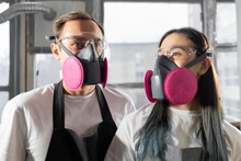 International couple man and woman in pink respirators in a workshop. Respiratory protection.