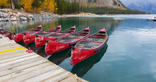 Red Boats Landing Near The Bank Of The Clear Blue Lake, Reflected In The Water. Mountain Lake With Moored Red Boats. Banff National Park, Canada. Travel Photo, Selective Focus, Blurred.