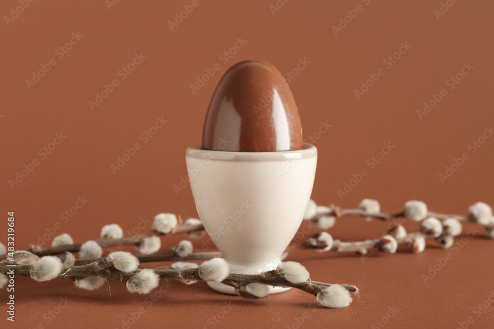Holder with chocolate Easter egg and willow branches on brown background