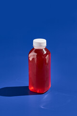 Berry lemonade in bottle on blue background. Drink in plastic bottle. Delivery drink. Trendy mock up bottle concept design. Drink container in minimal style.