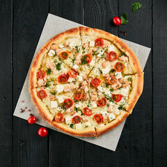 Sticker - Homemade salmon pizza on black wood background.  Pizza with salmon, tomatoes, dill and feta cheese on parchment. Italian food in rustic style. Junk food on dark background.