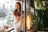 Fototapeta Tulipany - A young brunette girl in a cafe is warming herself near the fireplace, resting