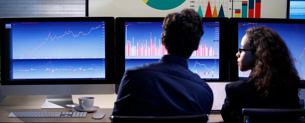 Closeup shot of big center monitor showing company analysis target circle graph and chart report in trading room full of computer screen while unrecognizable unknown male and female staff working