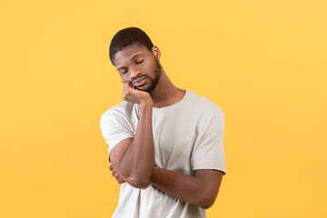 Tired african american guy leaning on his hand and sleeping after overworking, standing over yellow background