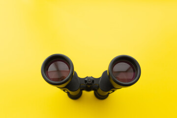 Binoculars on a light yellow background. Banner. Flat lay, top view.