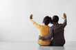 Millennial black family planning interior with raised hands up, sit on floor on gray wall background, empty space