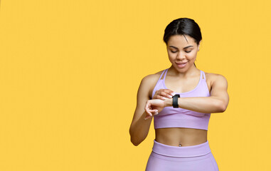 Wall Mural - Happy african american lady using smartwatch to monitor progress, checking her performance, yellow background