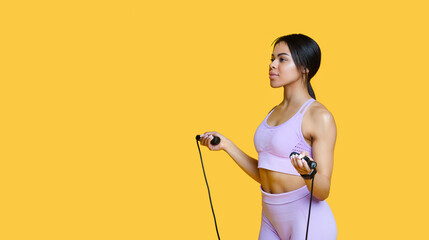 Wall Mural - Sporty african american woman with jump rope, wearing sportswear and ready for fitness training, yellow background