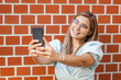 © BooNKer - Young girl taking a selfie - Smiling at the camera - Happy student standing by the wall and using her smartphone