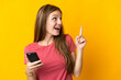 © luismolinero - Young woman using mobile phone isolated on yellow background intending to realizes the solution while lifting a finger up