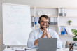 © Prostock-studio - Smiling mature caucasian male teacher with beard in glasses and headphones looking at laptop in living room