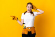 © luismolinero - Young electrician woman isolated on yellow background surprised and pointing finger to the side
