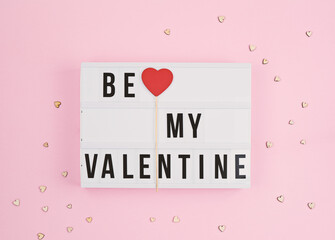 Valentine's day greeting card with light box text Be My Valentine love confession with wooden red heart stick, pink background