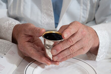 A Man Holds A Silver Cup And Recites The Blessing Over Wine During A Passover Seder. 