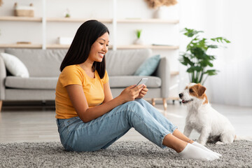 Wall Mural - Smiling asian lady checking photos of her puppy, using cellphone