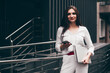 © Mykola - Beautiful young caucasian businesswoman in a white clothes with a laptop and notebook outdoor near business centre