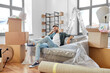 © Syda Productions - moving, people and real estate concept - happy smiling man with boxes resting on sofa covered with plastic sheeting at new home