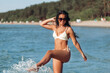 © Syda Productions - people, summer and leisure concept - happy young woman in bikini swimsuit playing with sea water on beach