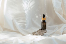 Amber Glass Bottle Of Essential Oil Or Serum With Pipette On White Fabric Background With Shadows. Natural Skincare Cosmetic Concept