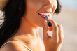 people, summer and swimwear concept - close up of happy smiling young woman in bikini swimsuit and straw hat applying lip balm on beach